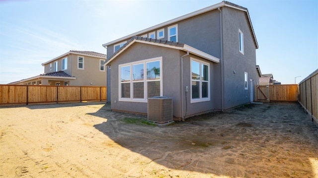 rear view of house with central AC unit, a fenced backyard, and stucco siding