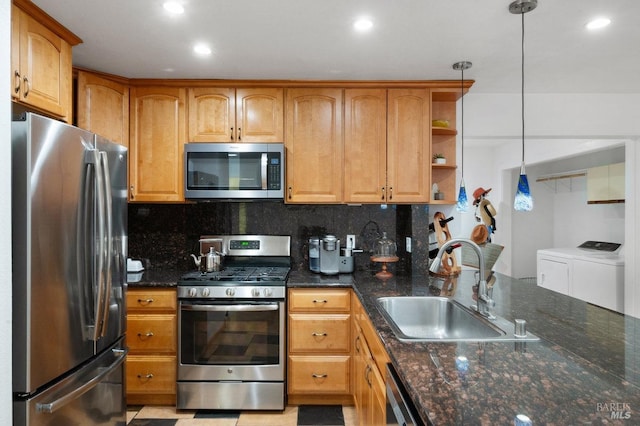 kitchen with stainless steel appliances, dark stone countertops, sink, decorative light fixtures, and washing machine and clothes dryer