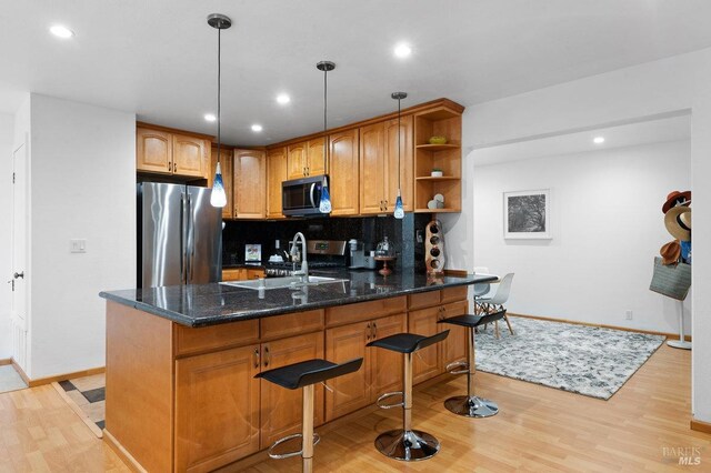 kitchen featuring decorative backsplash, hanging light fixtures, appliances with stainless steel finishes, light hardwood / wood-style flooring, and sink