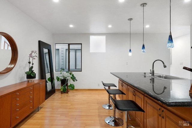 kitchen featuring a breakfast bar area, light wood-type flooring, dark stone counters, sink, and decorative light fixtures