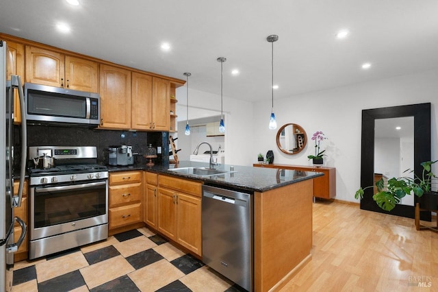 kitchen featuring appliances with stainless steel finishes, sink, kitchen peninsula, hanging light fixtures, and light hardwood / wood-style flooring