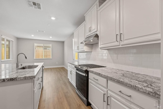 kitchen with tasteful backsplash, an island with sink, sink, white cabinets, and stainless steel range with gas stovetop