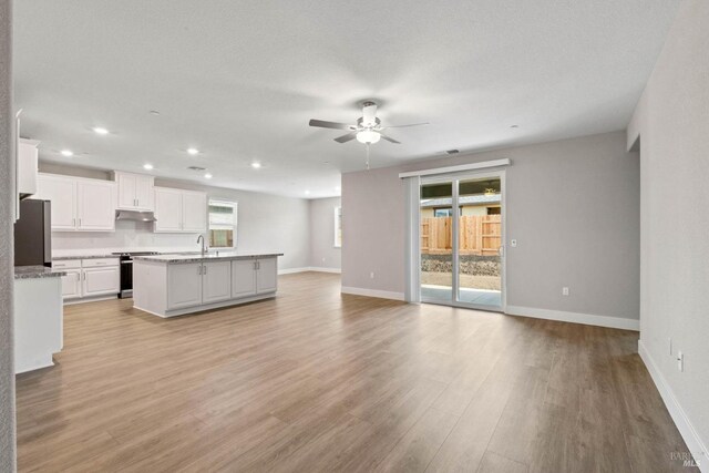 unfurnished living room featuring a textured ceiling, ceiling fan, sink, and light hardwood / wood-style flooring