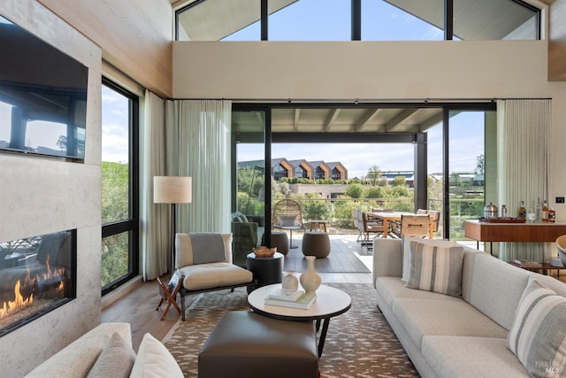 living room featuring a high ceiling, a glass covered fireplace, and wood finished floors