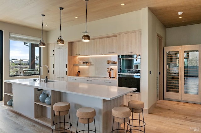 kitchen featuring light brown cabinetry, a sink, modern cabinets, open shelves, and a breakfast bar