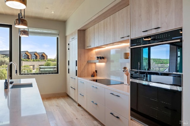 kitchen featuring a sink, black appliances, light wood-type flooring, modern cabinets, and light countertops