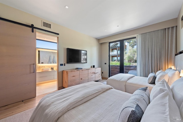 bedroom with a barn door, access to exterior, visible vents, light wood-style floors, and connected bathroom