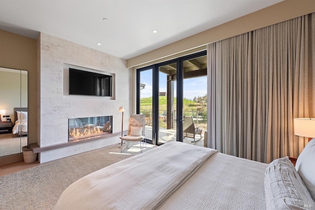 bedroom featuring recessed lighting, a glass covered fireplace, wood finished floors, and access to outside