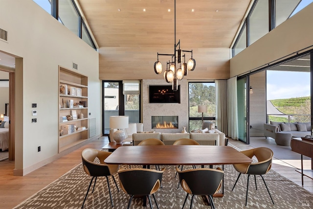 dining area with a towering ceiling, wooden ceiling, light wood-style floors, built in features, and a large fireplace