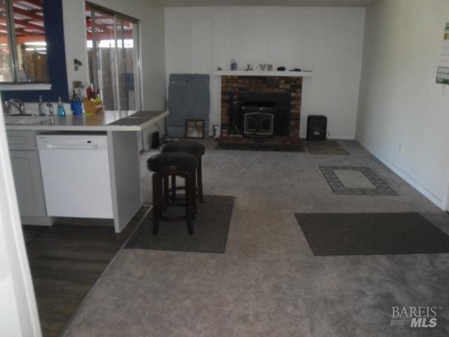 kitchen featuring sink, a kitchen bar, white dishwasher, a wood stove, and kitchen peninsula