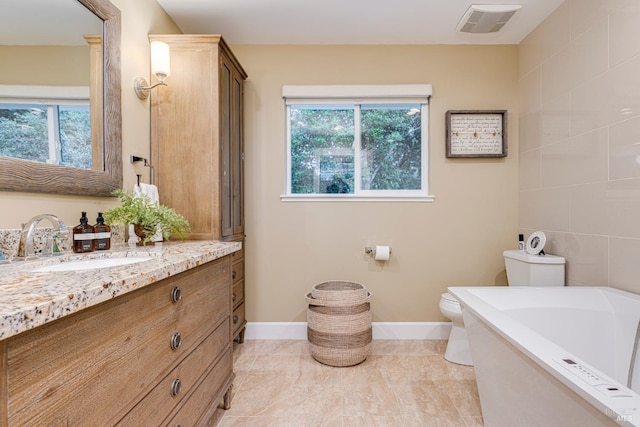 bathroom with toilet, a tub, a healthy amount of sunlight, and vanity