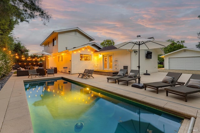 pool at dusk with french doors, a garage, outdoor lounge area, an outbuilding, and a patio