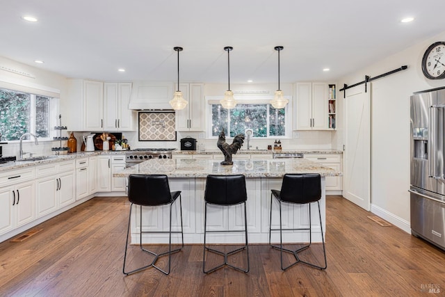 kitchen featuring dark wood-type flooring, sink, a barn door, appliances with stainless steel finishes, and light stone counters