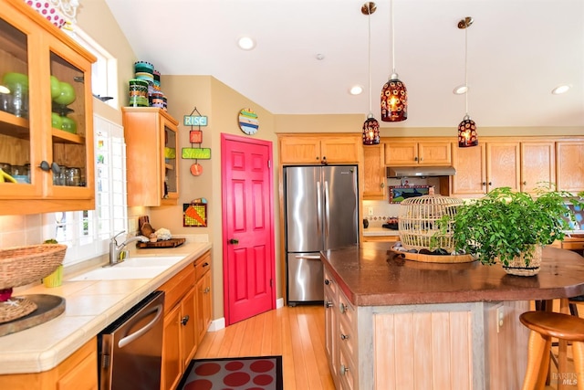 kitchen featuring appliances with stainless steel finishes, a sink, light wood finished floors, a center island, and under cabinet range hood