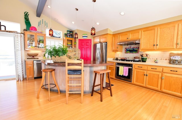 kitchen featuring vaulted ceiling with beams, a kitchen island, appliances with stainless steel finishes, and a kitchen bar