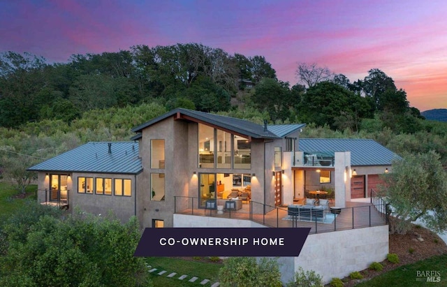 back house at dusk with a balcony and outdoor lounge area