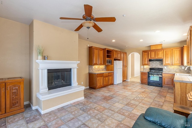 kitchen with black gas stove, backsplash, sink, white refrigerator, and ceiling fan