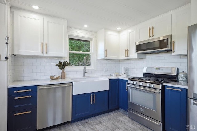 kitchen with white cabinets, blue cabinets, stainless steel appliances, light countertops, and a sink