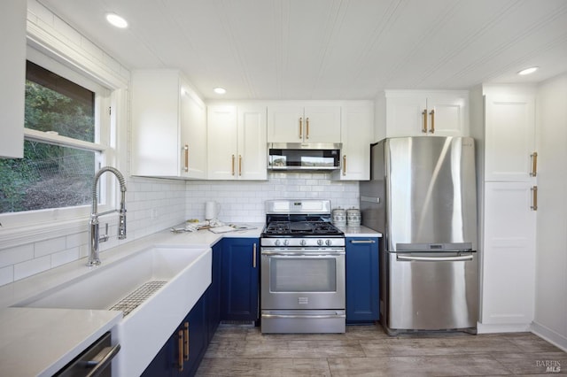 kitchen with a sink, white cabinets, light countertops, appliances with stainless steel finishes, and blue cabinetry