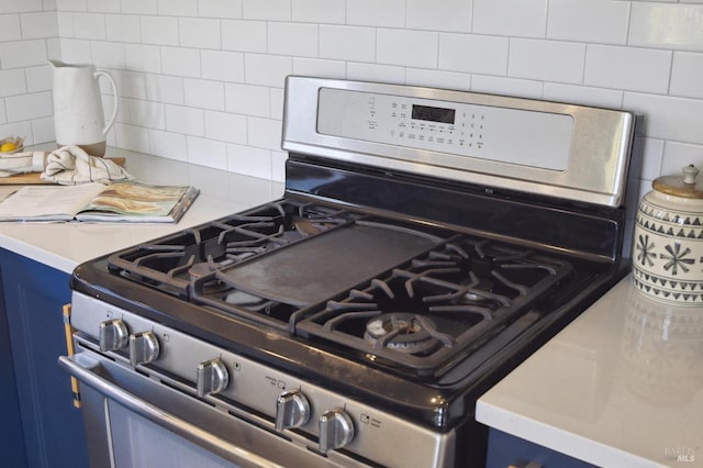 details with stainless steel gas stove, light countertops, blue cabinetry, and backsplash