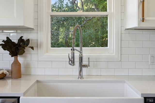 room details featuring light countertops, tasteful backsplash, a sink, and white cabinets