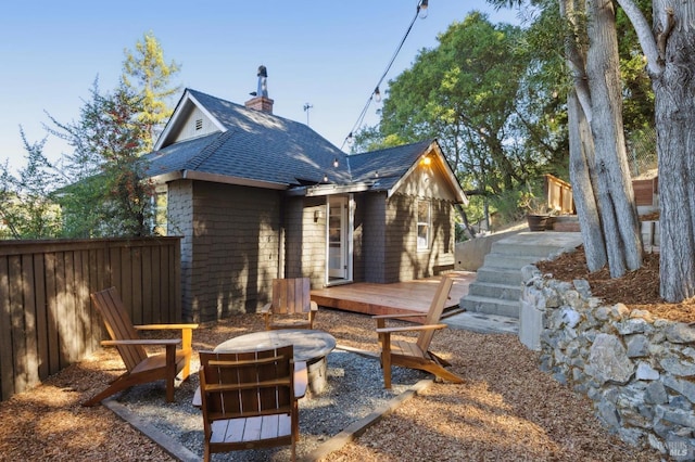 back of house featuring roof with shingles, a chimney, an outdoor fire pit, fence, and a deck