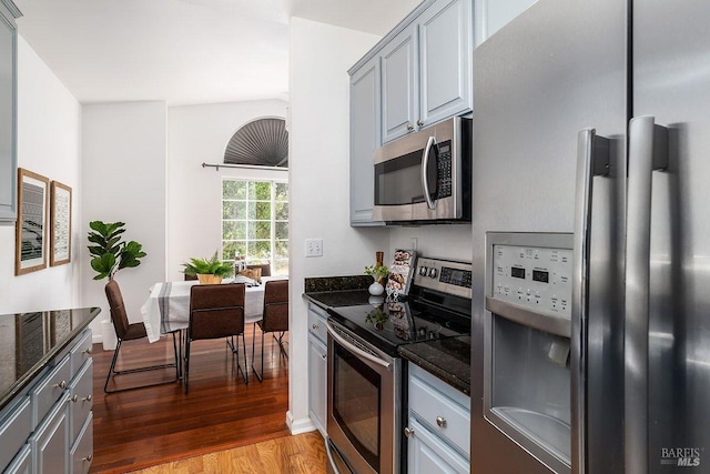 kitchen featuring gray cabinetry, stainless steel appliances, wood-type flooring, and dark stone countertops