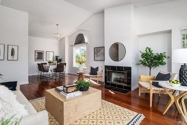 living room featuring an inviting chandelier, high vaulted ceiling, dark wood-type flooring, and a tile fireplace