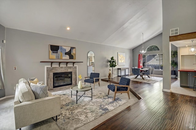 living room featuring vaulted ceiling, wood-type flooring, and a tiled fireplace