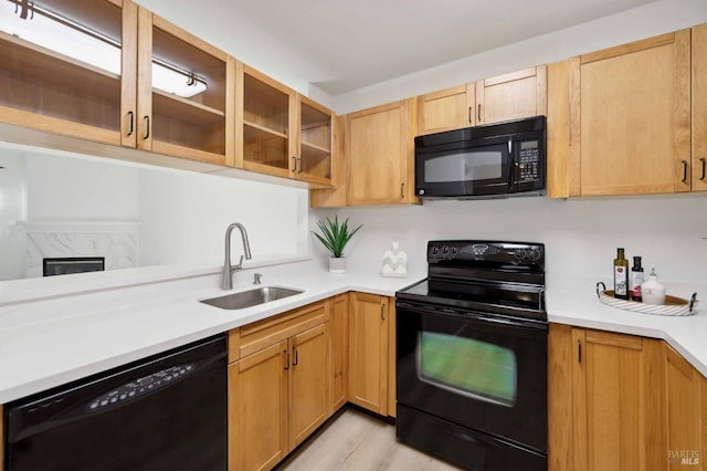 kitchen with light wood-type flooring, sink, black appliances, light brown cabinets, and a fireplace