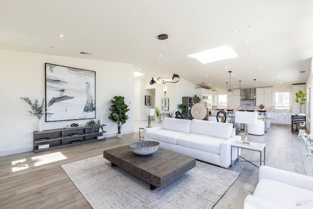 living room with lofted ceiling with skylight, a chandelier, and light wood-type flooring