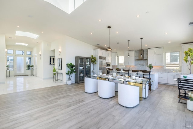 kitchen with a spacious island, white cabinetry, wall chimney range hood, and decorative light fixtures