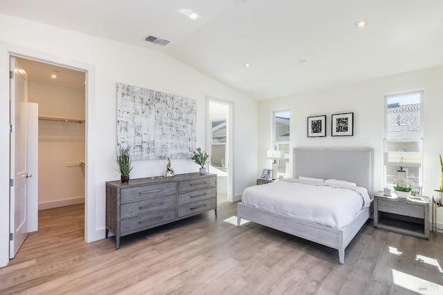 bedroom featuring light hardwood / wood-style floors, a walk in closet, a closet, and lofted ceiling