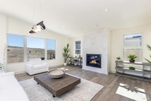 living room with lofted ceiling, a tiled fireplace, and light wood-type flooring