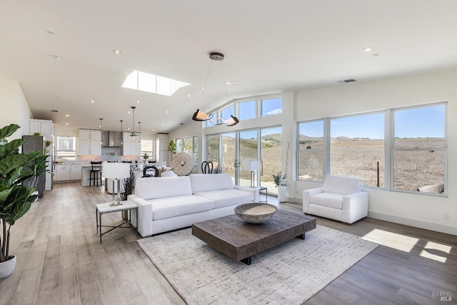 living room featuring a mountain view, an inviting chandelier, light wood-type flooring, high vaulted ceiling, and a skylight