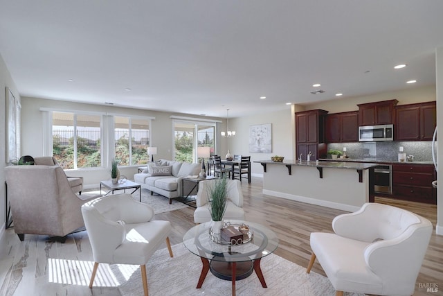 living room with an inviting chandelier, a healthy amount of sunlight, and light hardwood / wood-style flooring