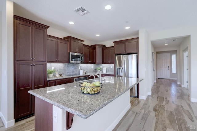 kitchen featuring stainless steel appliances, a center island with sink, a breakfast bar, light stone counters, and tasteful backsplash