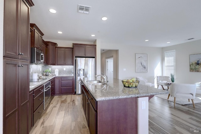 kitchen featuring tasteful backsplash, appliances with stainless steel finishes, sink, an island with sink, and light hardwood / wood-style floors