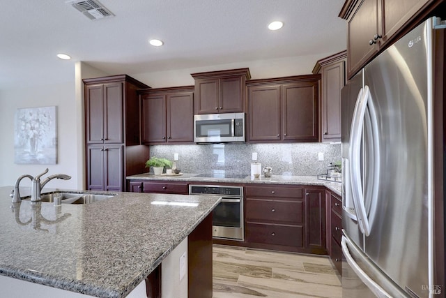 kitchen featuring appliances with stainless steel finishes, light stone counters, an island with sink, and backsplash