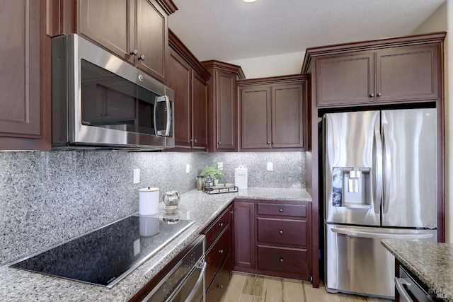 kitchen featuring appliances with stainless steel finishes, light hardwood / wood-style floors, backsplash, and light stone countertops