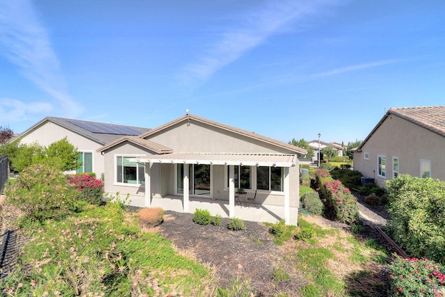 rear view of property featuring a patio area and solar panels