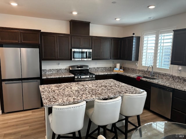 kitchen featuring stainless steel appliances, sink, a center island, light stone counters, and light hardwood / wood-style floors