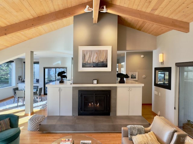 living room with beam ceiling, light hardwood / wood-style flooring, a tile fireplace, and wooden ceiling