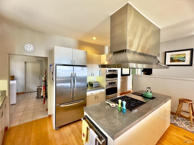 kitchen with washer / dryer, light wood-type flooring, stainless steel appliances, white cabinets, and exhaust hood