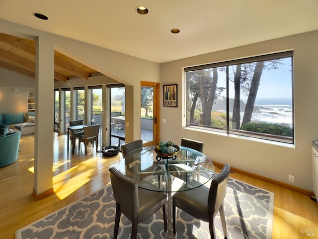 dining room with lofted ceiling with beams, a water view, and light wood-type flooring