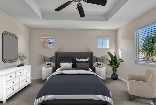 carpeted bedroom with ceiling fan, baseboards, and a raised ceiling