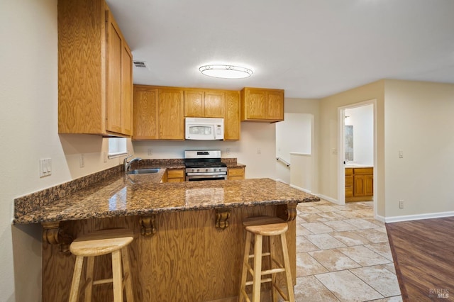 kitchen featuring sink, stainless steel gas stove, kitchen peninsula, light hardwood / wood-style floors, and dark stone countertops