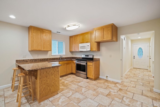 kitchen featuring a kitchen bar, stainless steel range with gas stovetop, kitchen peninsula, and sink