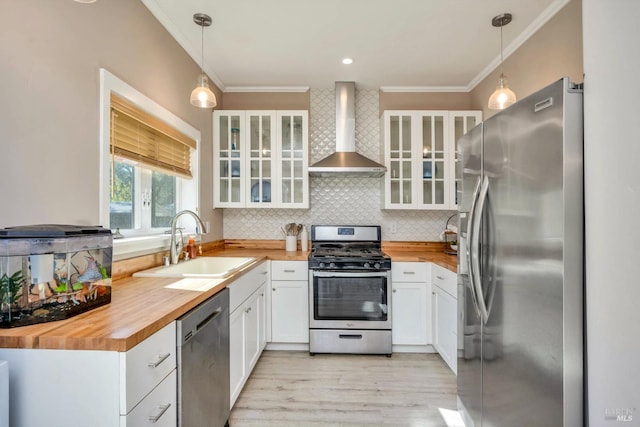 kitchen featuring appliances with stainless steel finishes, wall chimney exhaust hood, white cabinetry, and hanging light fixtures