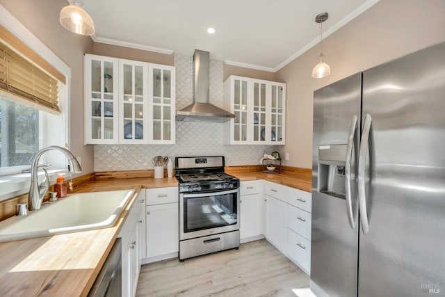 kitchen featuring wall chimney exhaust hood, stainless steel appliances, white cabinets, decorative light fixtures, and butcher block countertops